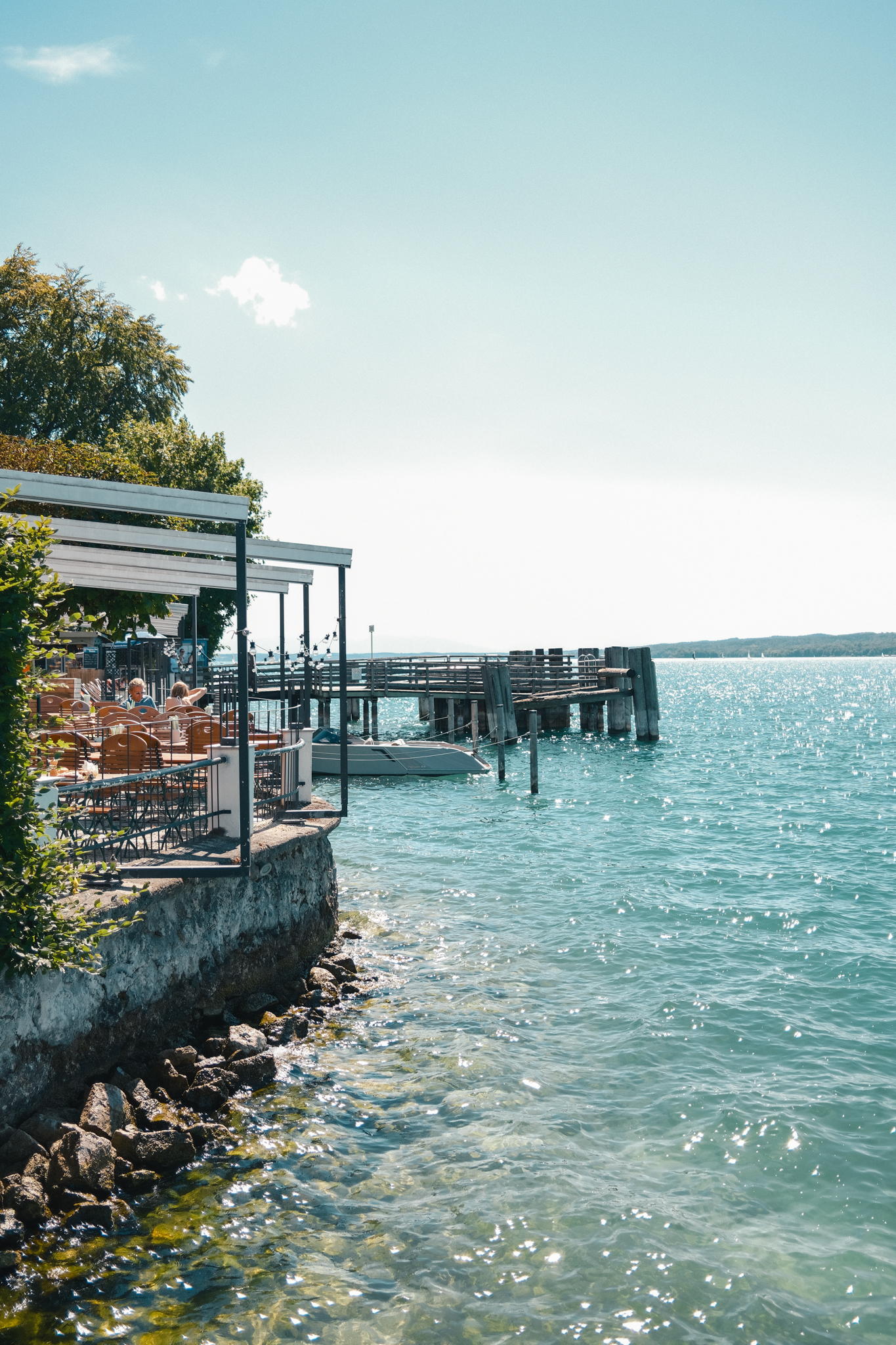 Die Seeterrasse des Strandhotel Berg mit Tischen unter Markisen, daneben der Bootssteg am Starnberger See
