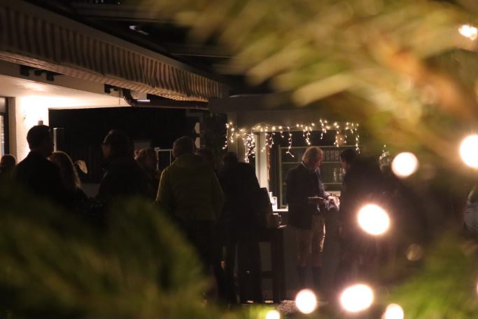 Eine große Menschenmenge steht im Hintergrund, davor sind weihnachtliche Lichter und Tannenzapfen zu sehen